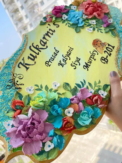 Holding the ornate "Kulkarni's" nameplate to showcase its unique shape and vibrant floral borders.