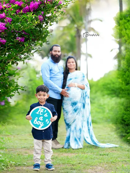 A proud older brother-to-be announces "It's a boy" with a custom sign. His parents stand in the background, creating a lovely family portrait that celebrates the upcoming arrival in our verdant outdoor space.