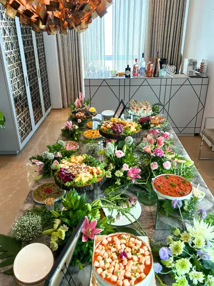 A fresh and vibrant grazing table perfect for a daytime event or brunch. This beautiful spread is filled with colorful salads, light bites, and fresh pizzas, surrounded by lush floral arrangements on a modern marble tabletop.