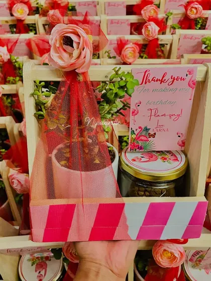 Flamingo-themed hampers are perfect for a tropical party. This one features a plant and a jar of treats in a wooden crate decorated with pink stripes and a floral touch.