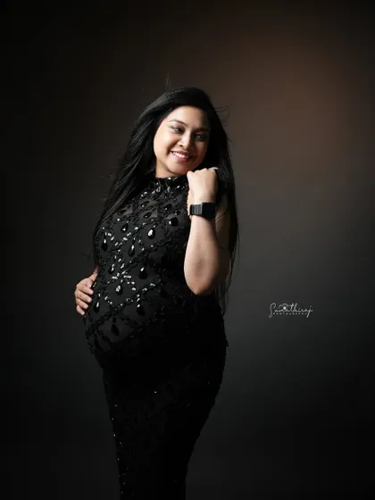 A joyful and candid shot of a mother-to-be in a black sequined gown. Her happy expression and the dynamic movement of her hair create a vibrant and glamorous portrait.