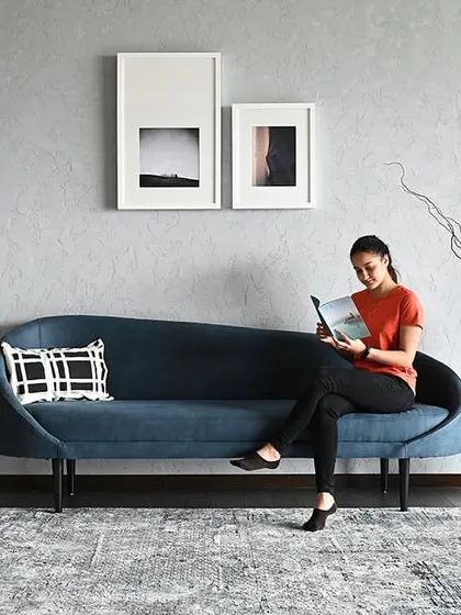 A person enjoying the lounge area, showing how the space is designed for human comfort. The curved blue sofa and soft lighting create a perfect spot to relax or read within the corporate environment.