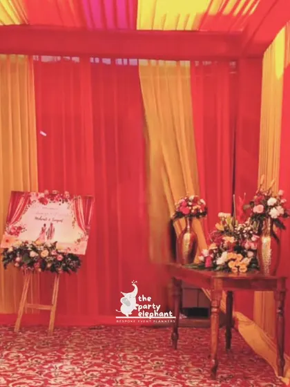 The entrance to the Mehendi ceremony, draped in vibrant red and yellow fabrics, with a custom welcome sign and floral arrangements setting a festive mood.