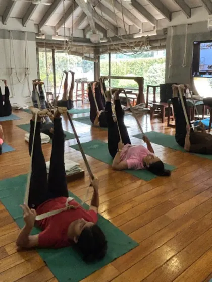 A class in session, with students using belts for Supta Padangusthasana. This shows the collective energy of a group practice, where everyone is on their own journey but supported by the community.