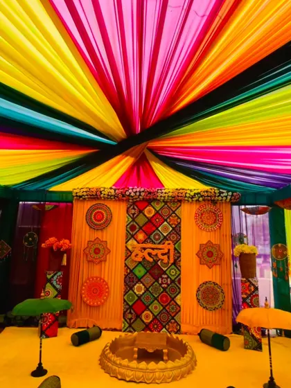 A traditional Haldi ceremony setup with a vibrant rainbow canopy. The backdrop features intricate patterns and the word 'Haldi' written in Hindi, blending tradition with a burst of color.