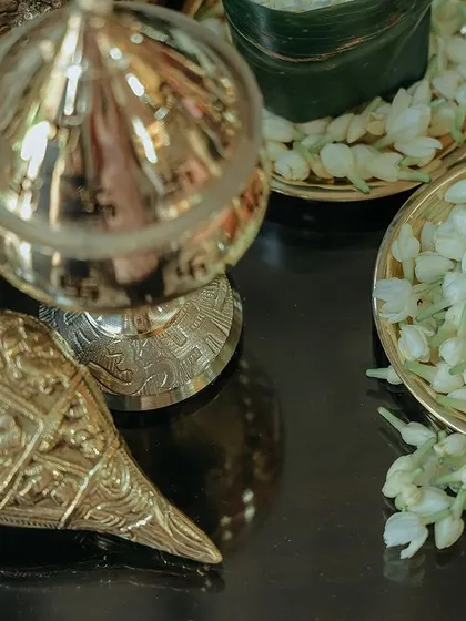 A close up of a brass conch shell (shankh) and a bowl of fresh jasmine buds. These items are central to Hindu rituals and add a layer of authenticity to the decor.