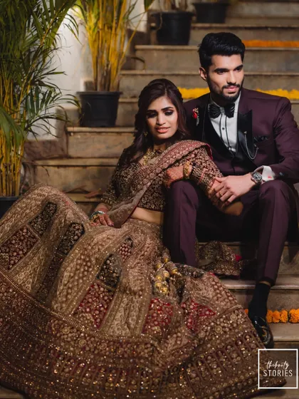 A regal portrait of the couple seated on a staircase. The bride's elaborate lehenga and the groom's sharp suit create a look of pure elegance for their reception.