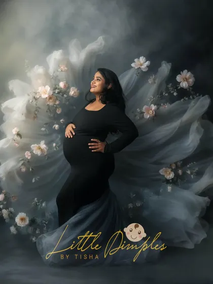 The beauty of motherhood captured in a dark, dreamy, and floral setting. The flowing grey fabric adds a touch of ethereal grace to this portrait.