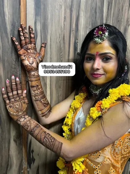 A happy bride during her haldi ceremony, showing off her full bridal mehendi which includes portraits and traditional wedding scenes.