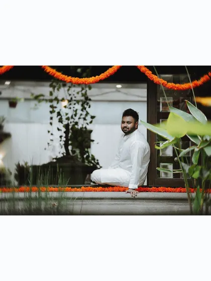 The groom sits casually on a windowsill adorned with marigold garlands, a relaxed and handsome portrait.