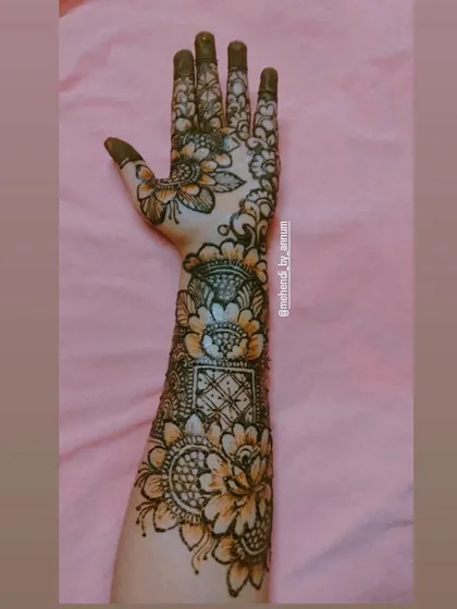 This full-arm design showcases a beautiful fusion of styles. It blends bold floral motifs with geometric squares and delicate vine patterns on the fingers, offering a modern twist on traditional bridal henna.