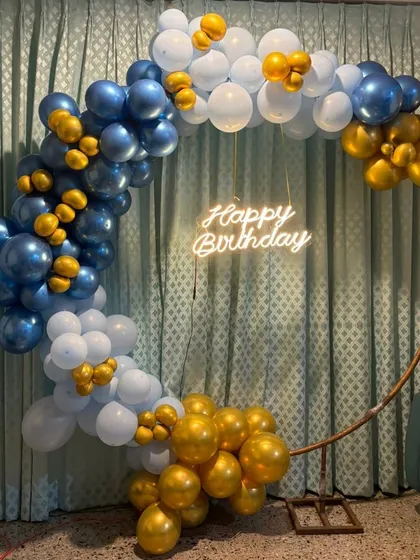 Our classic ring garlands are perfect for any occasion. This design features a stylish half-arch of royal blue, white, and gold chrome balloons on a copper-colored ring, finished with a 'Happy Birthday' neon sign for a clean and celebratory look.