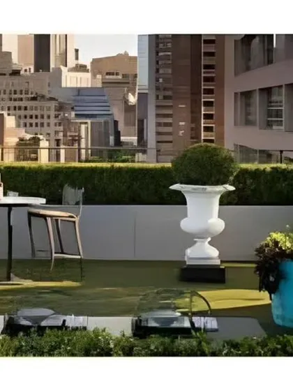 A luxurious rooftop terrace with a stunning city view. The space is designed for entertaining, featuring an outdoor grill, bar-height seating, and manicured hedges for privacy.