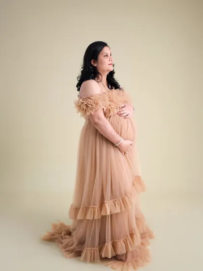 A simple yet stunning portrait in a nude-toned ruffled gown. The clean background keeps the focus entirely on the expecting mother and the elegant dress.