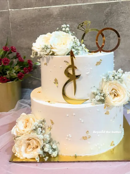 A full view of this elegant Nikkah cake, showcasing the two tiers, custom toppers, and the graceful arrangement of fresh white roses.