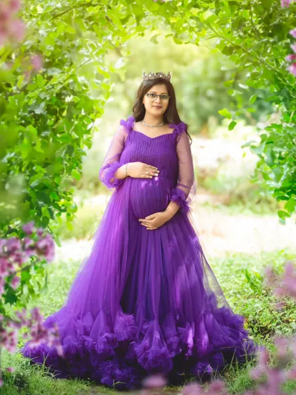 A regal outdoor portrait of a mom-to-be wearing a crown and a magnificent purple gown, surrounded by nature's beauty.