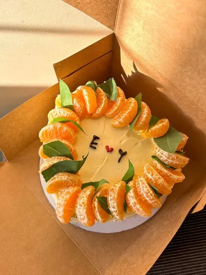 A rustic and minimal heart-shaped cake. It's decorated with a crown of fresh mandarin orange slices and leaves, with simple initials in the center for a personal touch.
