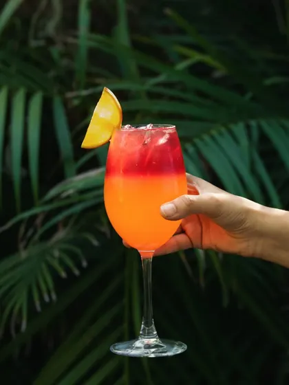 A vibrant, layered mocktail held against a lush, green background. This lifestyle shot connects the drink to a tropical, refreshing vibe, perfect for a cafe with outdoor seating.