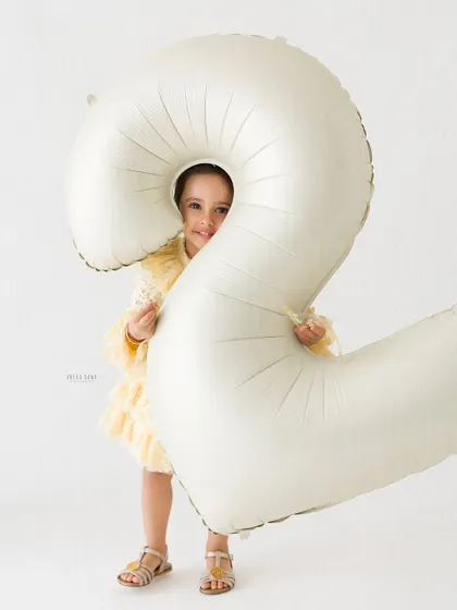 A fun and playful shot of a two-year-old peeking out from behind a giant birthday balloon. Her shy smile is absolutely precious.