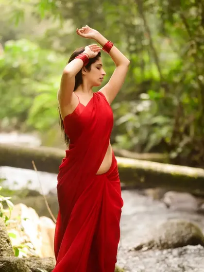 A side view of the red saree in the forest, capturing a moment of quiet contemplation. The natural light filtering through the trees creates a soft and ethereal mood.