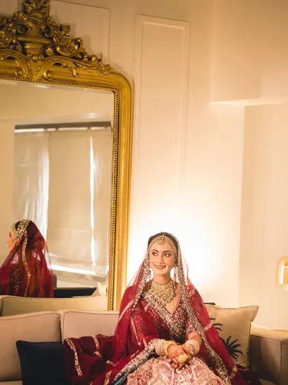 A wide portrait of the bride in her getting-ready room, the grand mirror reflecting her elegance.