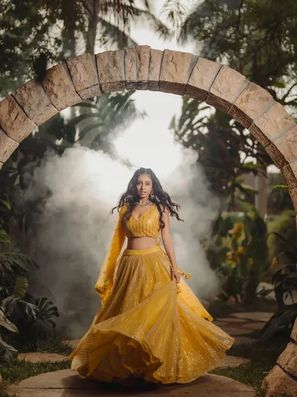 A fashion portrait that blends traditional wear with a touch of magic. The flowing yellow lehenga is set against a misty, atmospheric background, creating a cinematic and memorable image for a designer lookbook or model portfolio.