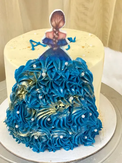 A beautiful princess gown cake. The dress is created with intricate blue whipped cream piping, giving it a flowing, floral texture.