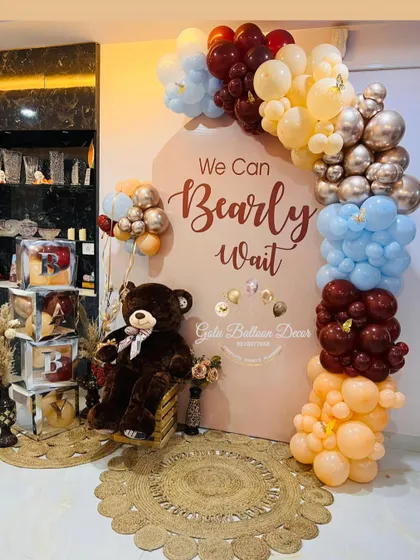A "We Can Bearly Wait" baby shower backdrop for a home party, featuring a beautiful balloon arch in blue, brown, and cream.