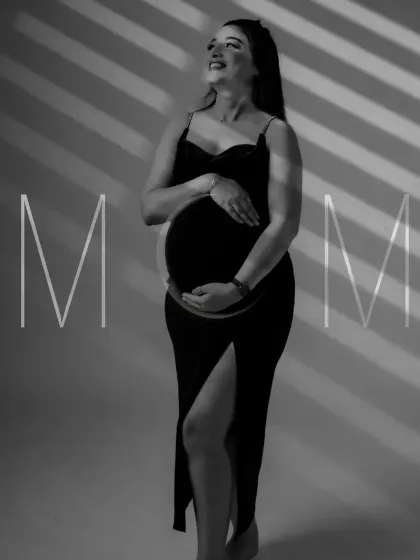 An artistic black and white portrait using creative lighting. The shadows create a striped pattern on the mom-to-be, highlighting her form in a unique and modern way.