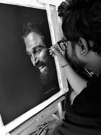 A black and white photo of me at work on the Allu Arjun portrait. This behind-the-scenes shot shows the process of building up layers of charcoal to achieve a realistic likeness.