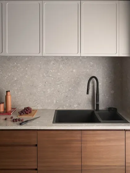The kitchen features handleless lower cabinets in a teak finish and upper cabinets in a light grey duco finish. This two-tone approach adds visual interest while keeping the space feeling bright.