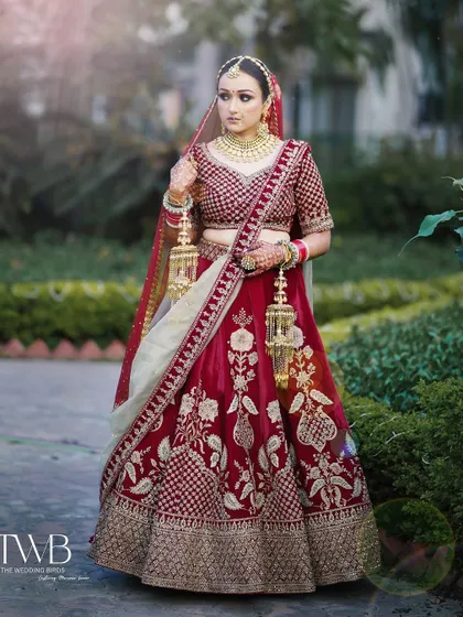 A full-length portrait showcasing the bride's magnificent wedding lehenga. Standing gracefully in a garden, she holds her kalire, embodying the timeless elegance of an Indian bride.