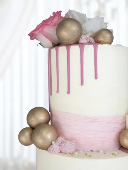 The top tier of this wedding cake, showing the beautiful contrast between the pink drip, golden spheres, and fresh white and pink roses.