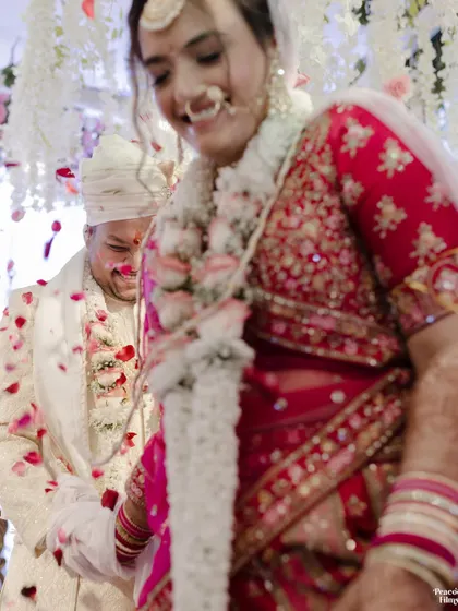 A candid, joyful moment of the couple during their wedding ceremony, their laughter captured amidst a shower of petals.