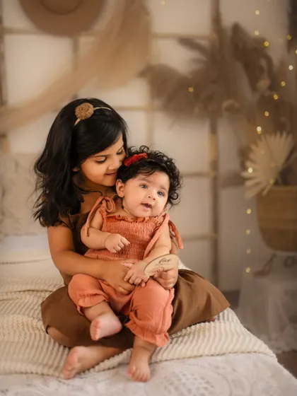 A tender moment between sisters during a five-month boho-themed milestone shoot. The warm, earthy tones and soft textures create a cozy and loving atmosphere.