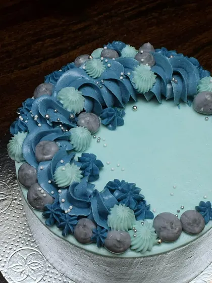 A close-up of the buttercream details on the light blue cake. You can see the different shapes and textures created by the piping, accented with tiny silver pearls.