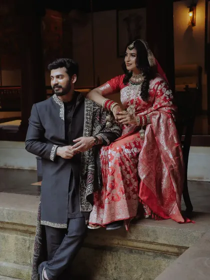 A regal portrait of a couple in traditional attire, posing on the steps of a classic building.