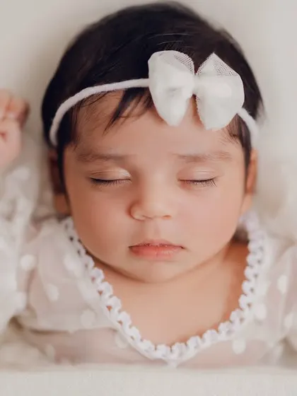 A close-up of a sleeping newborn, showcasing her delicate features and the soft lace of her dress. These simple, clean shots are all about capturing the pure innocence of a new life.