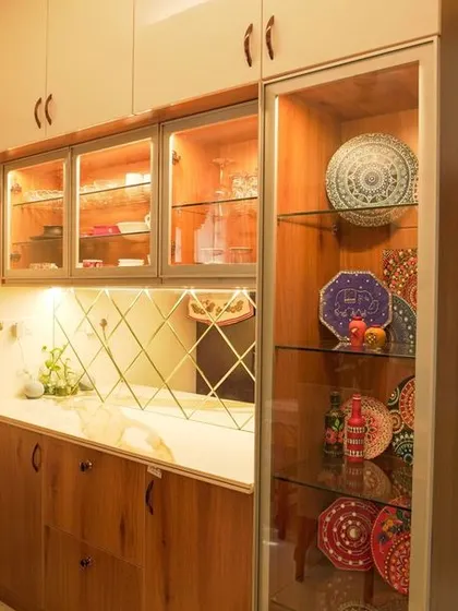 A close-up of a crockery unit next to the refrigerator, showcasing how we integrate storage solutions seamlessly into the home's layout. The glass doors and internal lighting add a touch of elegance.