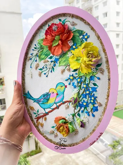 Holding the bird-themed oval panel to show its size and vibrant colors in natural light.