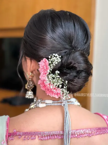 A side view of a classic low bun, beautifully decorated with pink carnations and baby's breath. This angle shows how the flowers are layered to create a lush, full effect.