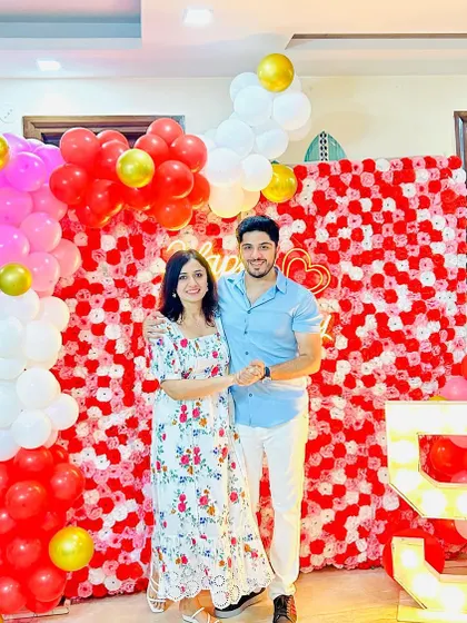 A 5th-anniversary home decoration with a red, pink, and white paper flower wall. The setup includes a balloon arch and a marquee number '5'.