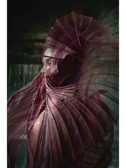 This image frames the model's face within the swirling form of a purple couture garment. This composition creates a sense of intimacy and mystery, perfect for a high-fashion brand.