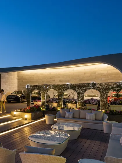 As evening descends, the outdoor lounge area of "The Rising Wave" becomes a magical space. The architectural lighting highlights the curved forms of the building and the meticulously landscaped gardens, perfect for hosting guests.