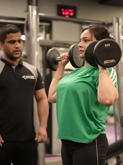 A trainer watches closely as a client performs a shoulder press, ensuring her form is correct to build strong, healthy shoulders.