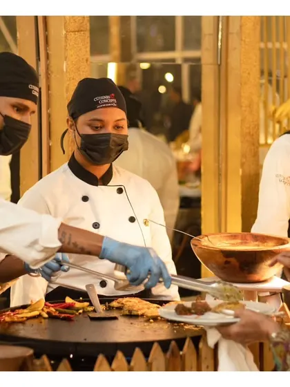 A female chef serving a guest from a large tawa, highlighting the skill and diversity of our culinary team.