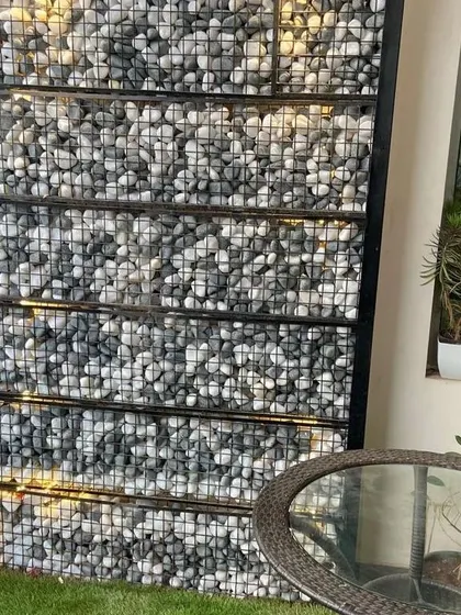 A detailed look at the illuminated gabion wall. The combination of industrial wire mesh, natural stones, and warm backlighting creates a unique feature that is both rustic and modern.
