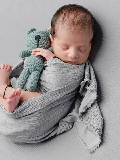 A perfectly swaddled newborn cuddling a tiny teddy bear. Using simple props and a neutral grey backdrop keeps the focus entirely on your baby's peaceful expression and tiny features.