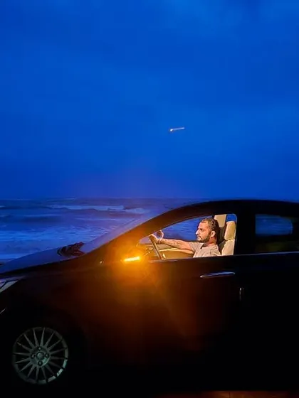 A cinematic night shot of my car parked by the sea, with the deep blue of the twilight sky meeting the ocean waves. This captures the moody, reflective feeling of a solo beach journey.