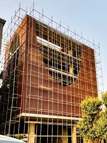 The "Shang Chi Cafe" building during the finishing stage of construction. The scaffolding highlights the large, curved void in the facade, showing the translation of a complex design element from drawing to physical form.
